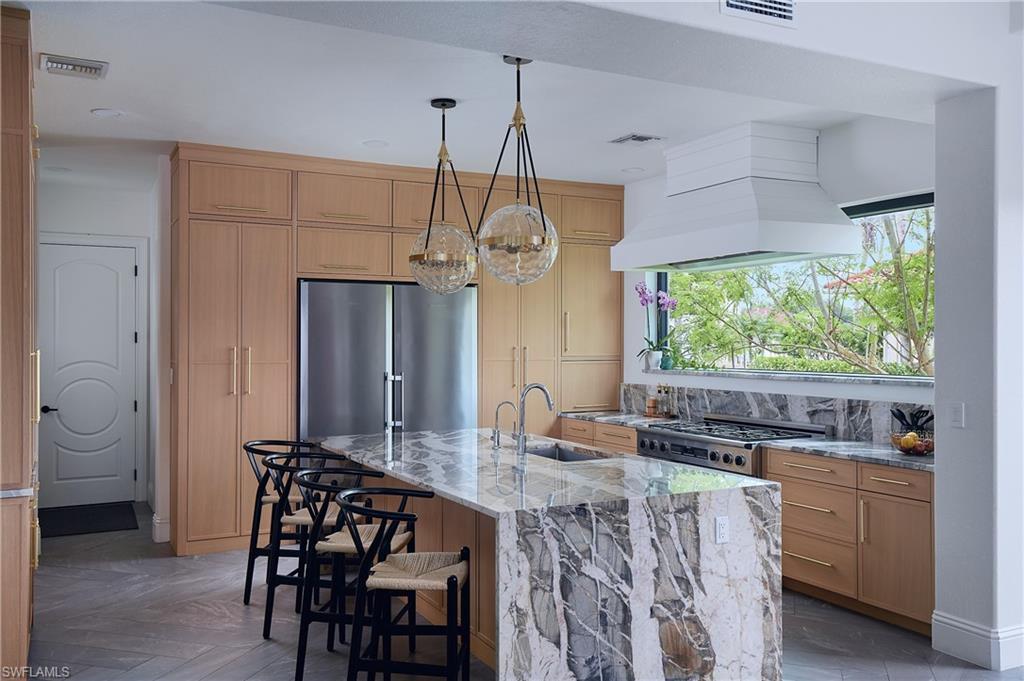 Image 4: Kitchen featuring a waterfall island with marble countertop, wood-finish cabinetry, stainless steel refrigerator, and recessed lighting