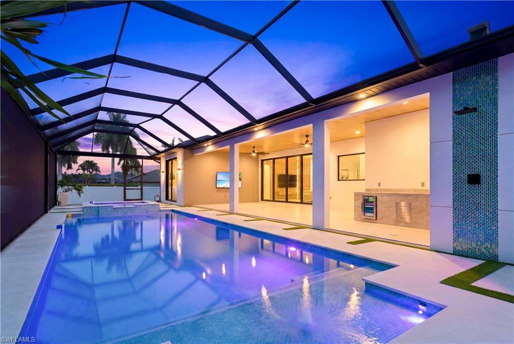 Image 4: Resort-style screened lanai with a heated pool and spa, sun shelf, outdoor kitchen, covered lounge area, and dramatic waterfall wall - beautifully lit for evening entertaining!