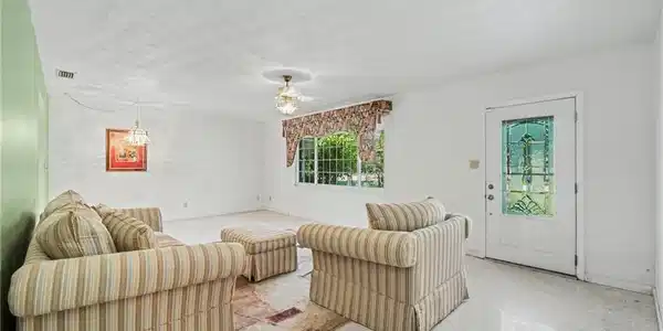 Image 3: Bright living space featuring a decorative glass-paneled entry door, a large window with exterior greenery visible, and a ceiling fan with light fixture