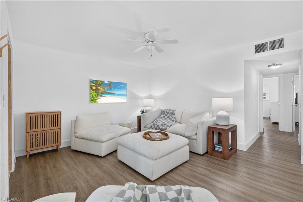 Image 3: Spacious living area featuring light wood-finish flooring, white walls, and a ceiling fan