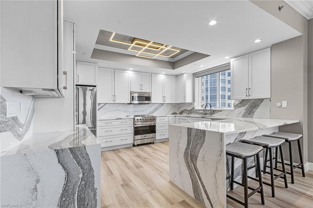 Image 4: Kitchen with light hardwood / wood-style floors, appliances with stainless steel finishes, tasteful backsplash, and a tray ceiling