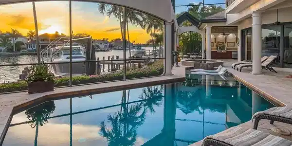 Image 3: Pool at dusk featuring glass enclosure, a patio, a sunroom, a pool with connected hot tub, and a water view