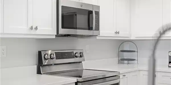 Image 4: Kitchen with stainless steel appliances, white cabinets, and light stone countertops