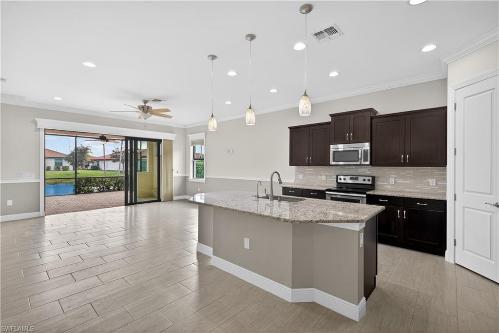Image 4: Kitchen with large island, pendant light fixtures, granite counters, tile backsplash, stainless steel appliances, pantry and tranquil water views.