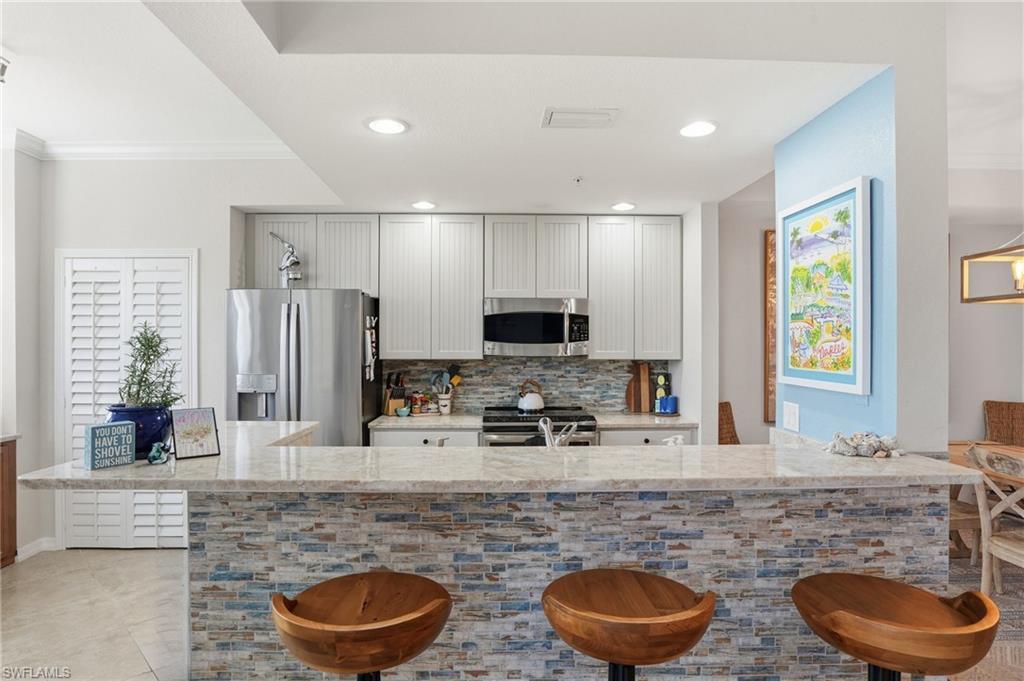 Image 2: Kitchen with light stone countertops, a kitchen breakfast bar, stainless steel appliances, tasteful backsplash, and recessed lighting