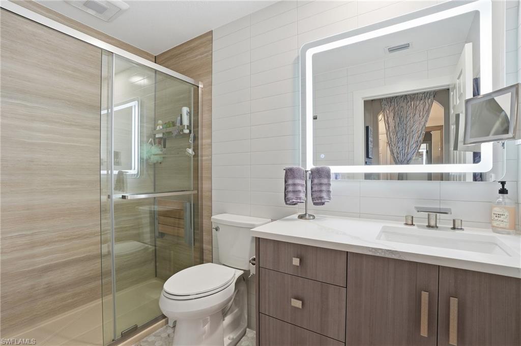 Image 3: Bathroom with vanity, a shower stall, tile walls, and decorative backsplash