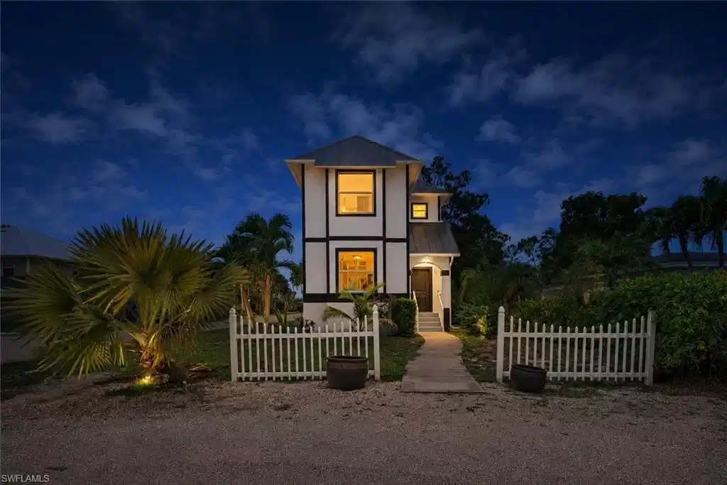 Image 1: Two-story residence featuring white siding with dark trim, a metal roof, and lighted windows