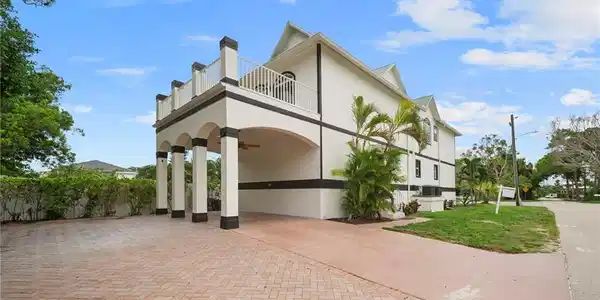 Image 2: Exterior with elevated balcony, columned porte-coch&egrave;re, paver driveway, stucco finish, and mature landscaping