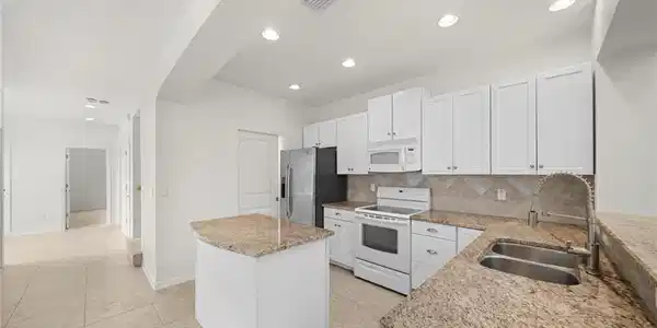 Image 4: Bright kitchen featuring white cabinetry, granite countertops, stainless steel appliances, a center island, and tile flooring