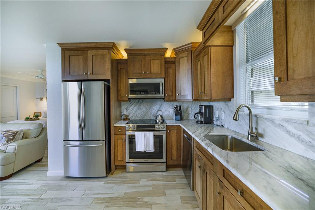 Image 3: Kitchen featuring stainless steel appliances, light stone countertops, wood finish cabinetry, and ceiling fan
