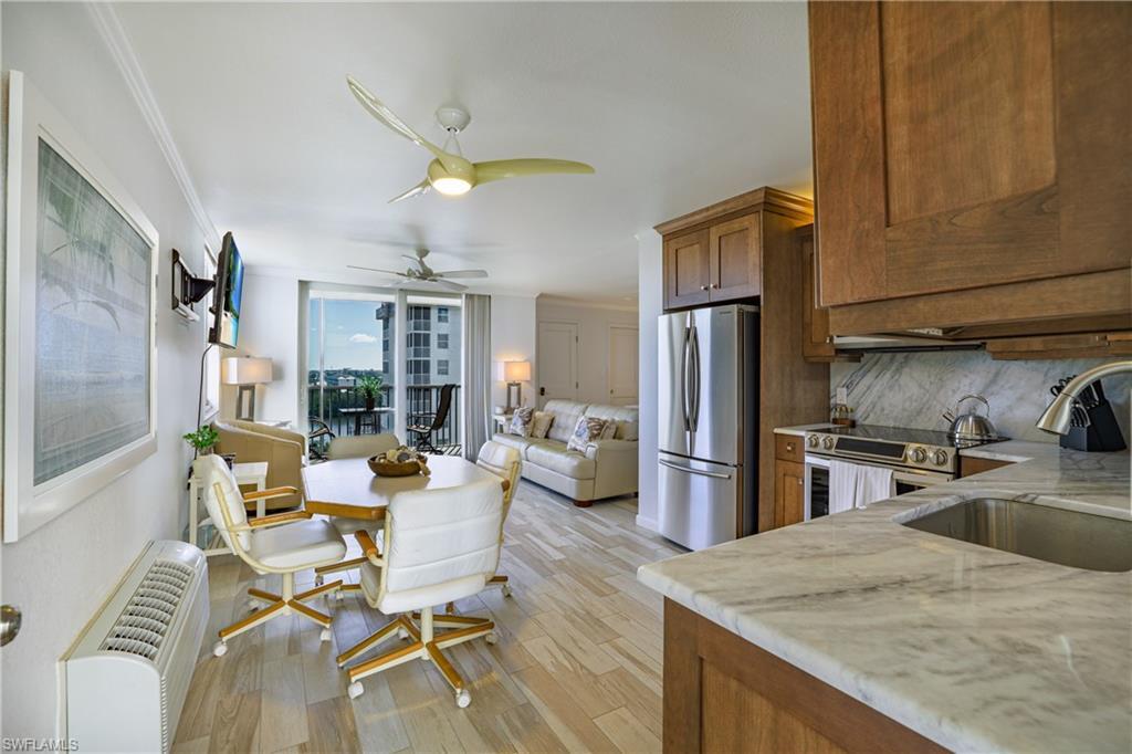 Image 4: Kitchen with stainless steel appliances, wood finish cabinetry, light wood-style flooring, open floor plan, and light stone countertops