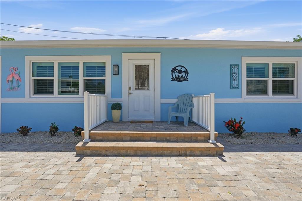 Image 2: Light blue exterior with white trim, featuring a paver driveway, matching paver porch steps, white railing, and a window with blinds - Virtually Edited Image