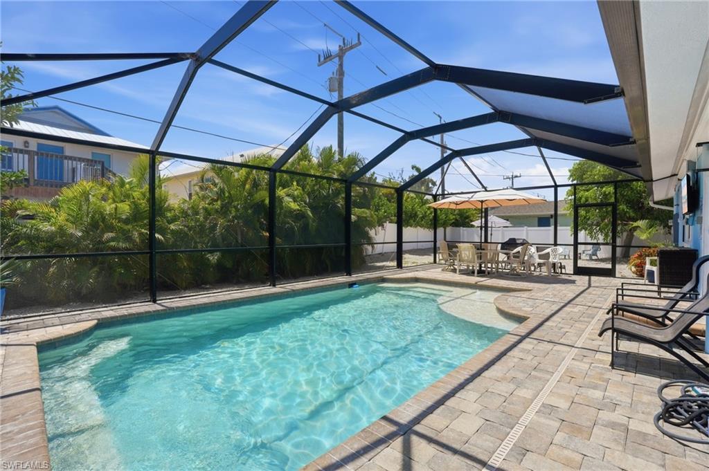 Image 4: Screened swimming pool area with paver decking, integrated sun shelf, and mature perimeter landscaping - Virtually Edited Image