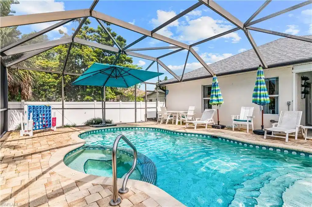 Image 1: Screened pool enclosure featuring an integrated spa with a curved entry, surrounded by paver decking and a white perimeter fence