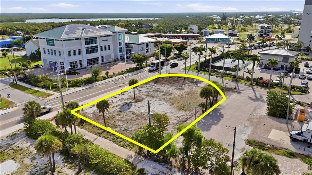 Image 4: Vacant lot with street frontage, featuring mature palm trees and direct proximity to established commercial structures - Virtually Edited Image