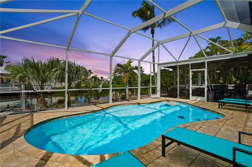 Image 1: Swimming pool featuring a screened  lanai and a canal view- Virtually Edited Image