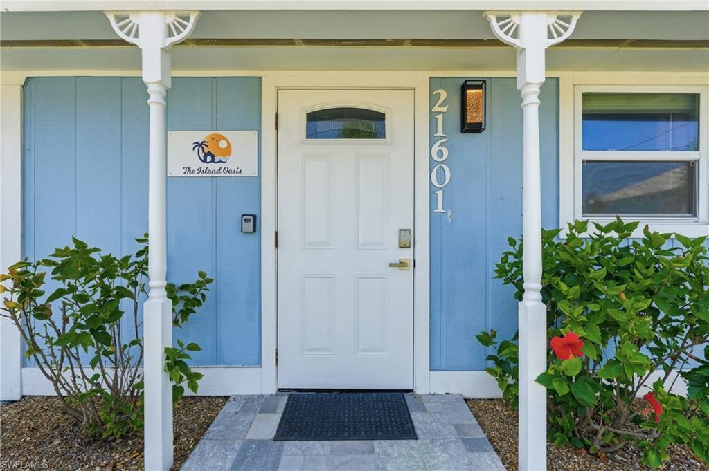 Image 4: Entryway featuring a paneled door with an arched window, light blue siding, and white architectural columns - Virtually Edited Image