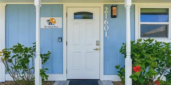 Image 4: Entryway featuring a paneled door with an arched window, light blue siding, and white architectural columns - Virtually Edited Image