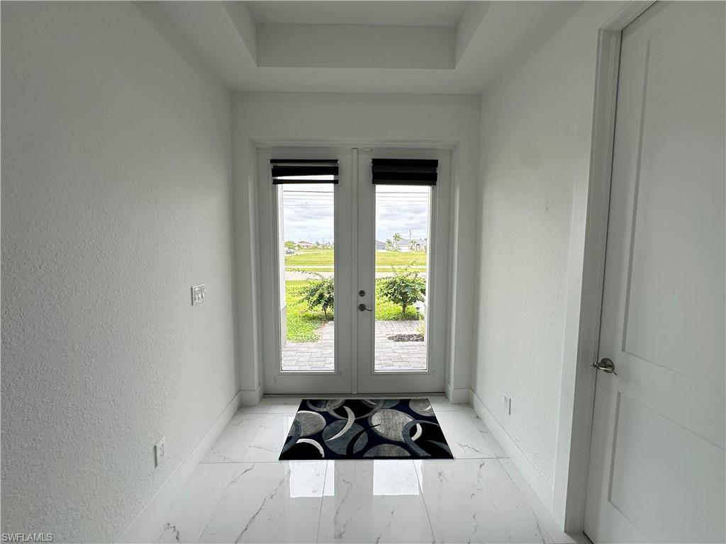 Image 4: Entryway featuring double French doors, large format tile flooring, a tray ceiling, and white panel doors