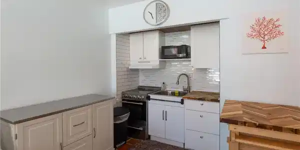 Image 4: Compact kitchen area featuring white cabinetry, a subway tile backsplash, and a stainless steel sink with a gooseneck faucet