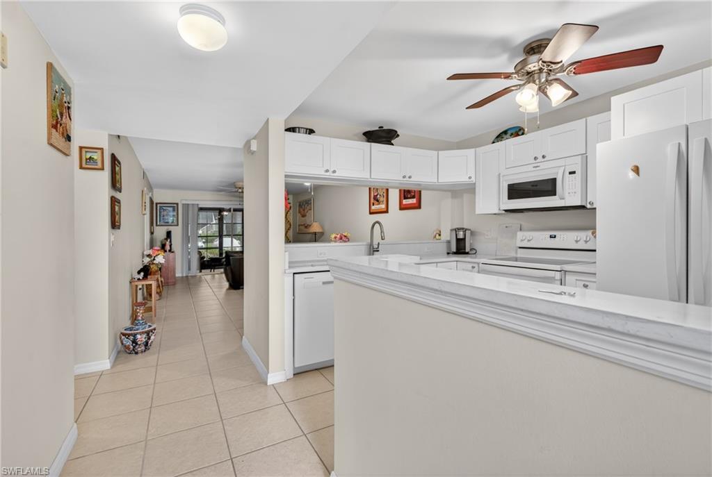Image 3: Bright kitchen featuring white cabinetry, a built-in microwave, white appliances, and a ceiling fan
