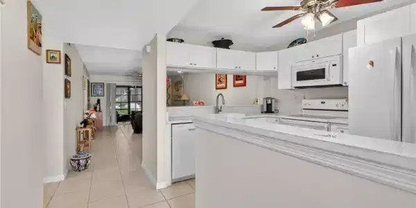 Image 3: Bright kitchen featuring white cabinetry, a built-in microwave, white appliances, and a ceiling fan