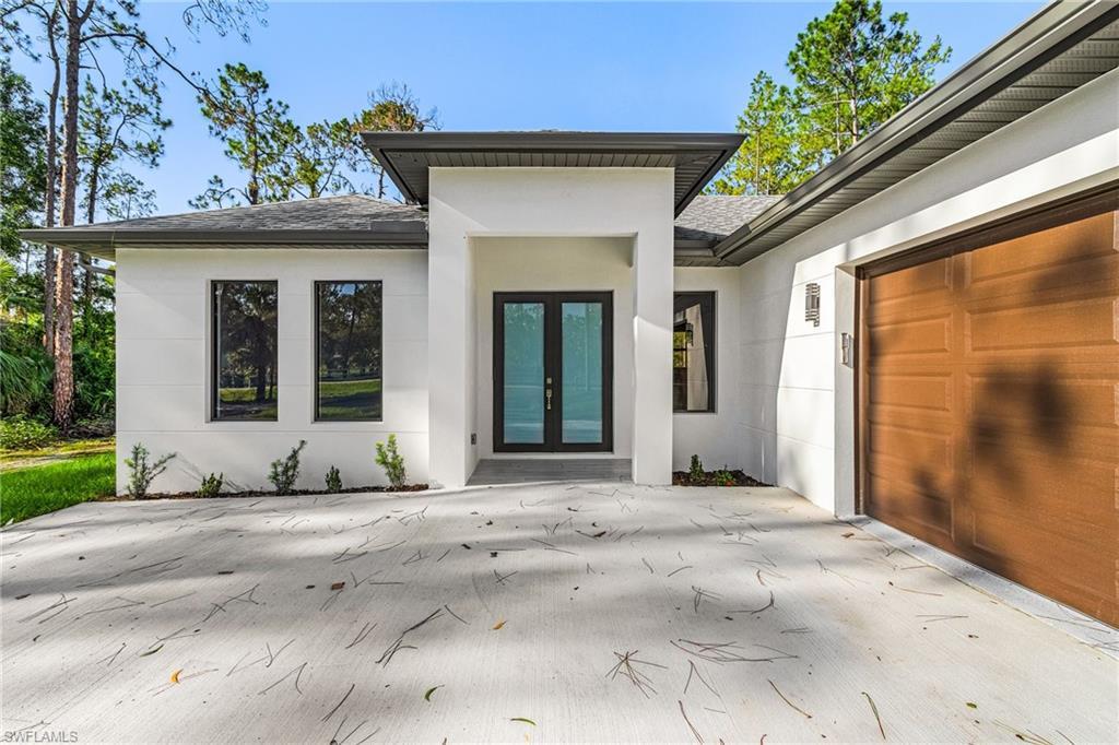 Image 3: Modern architectural exterior featuring a prominent covered entryway, double glass panel entry doors, a wood-finish garage door, and dark-framed windows
