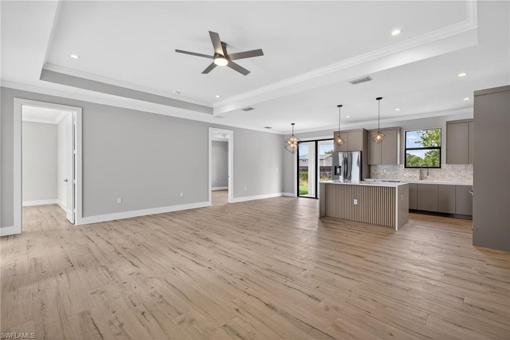 Image 4: Spacious open-concept interior featuring wood-look flooring, tray ceilings with recessed lighting, and a contemporary ceiling fan