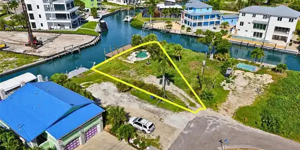 Image 4: Waterfront property featuring a private boat dock, an in-ground pool, mature palm trees, direct canal access, and a paved road approach - Virtually Edited Image