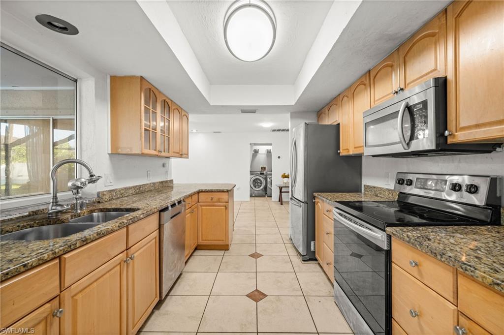 Image 3: Kitchen featuring stainless steel appliances, cabinets, a raised ceiling, dark stone counters, and light tile patterned flooring