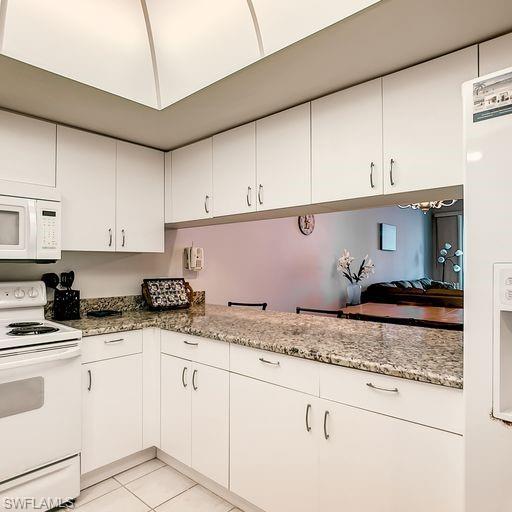 Image 2: Kitchen featuring white appliances, white cabinetry, light tile patterned flooring, and light stone countertops