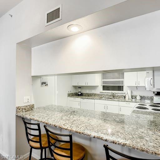 Image 4: Kitchen featuring white cabinets, light stone counters, and a breakfast bar area