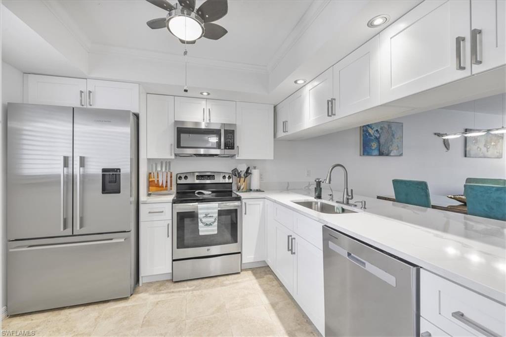 Image 1: Kitchen featuring appliances with stainless steel finishes, white cabinets, ornamental molding, a ceiling fan, and light stone counters