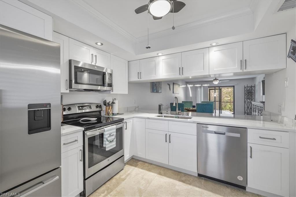 Image 3: Kitchen featuring a ceiling fan, appliances with stainless steel finishes, white cabinets, ornamental molding, and a raised ceiling