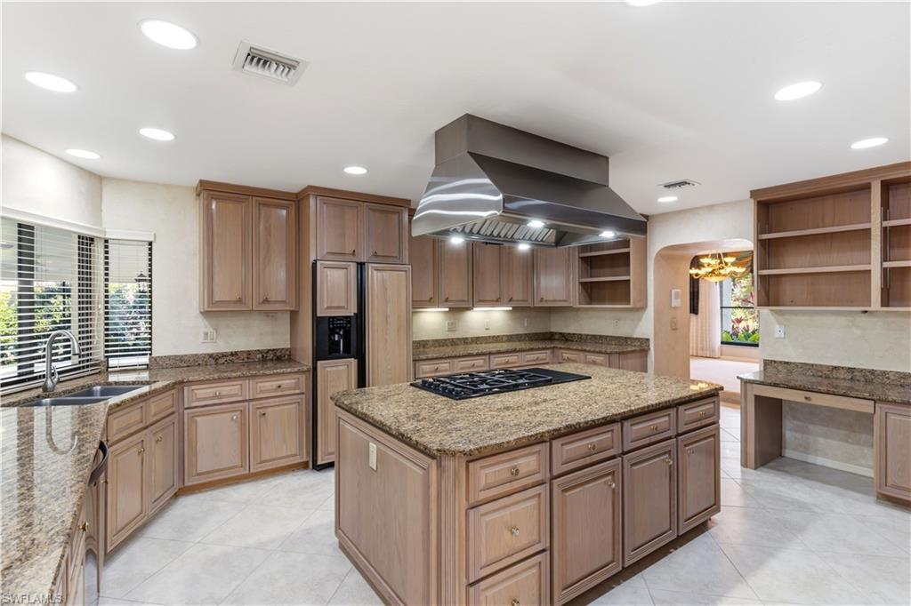 Image 4: Kitchen with exhaust hood, a center island, light stone counters, open shelves, and paneled built in refrigerator