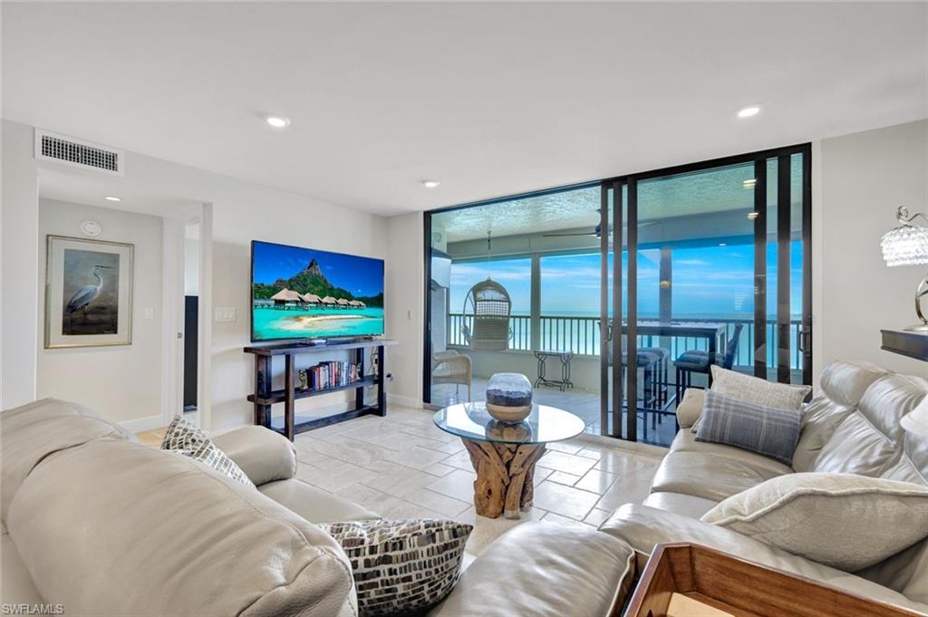 Image 4: Living room with a ceiling fan, expansive windows, and stone tile flooring