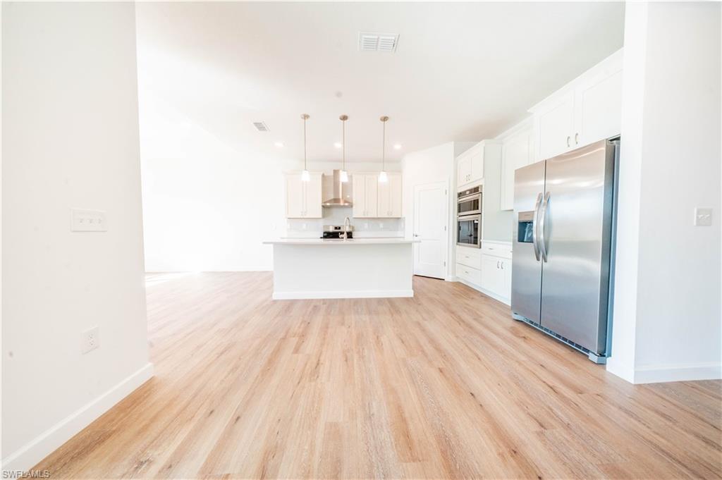 Image 4: Kitchen featuring stainless steel appliances, white cabinetry, light countertops, pendant lighting, and light wood-style floors