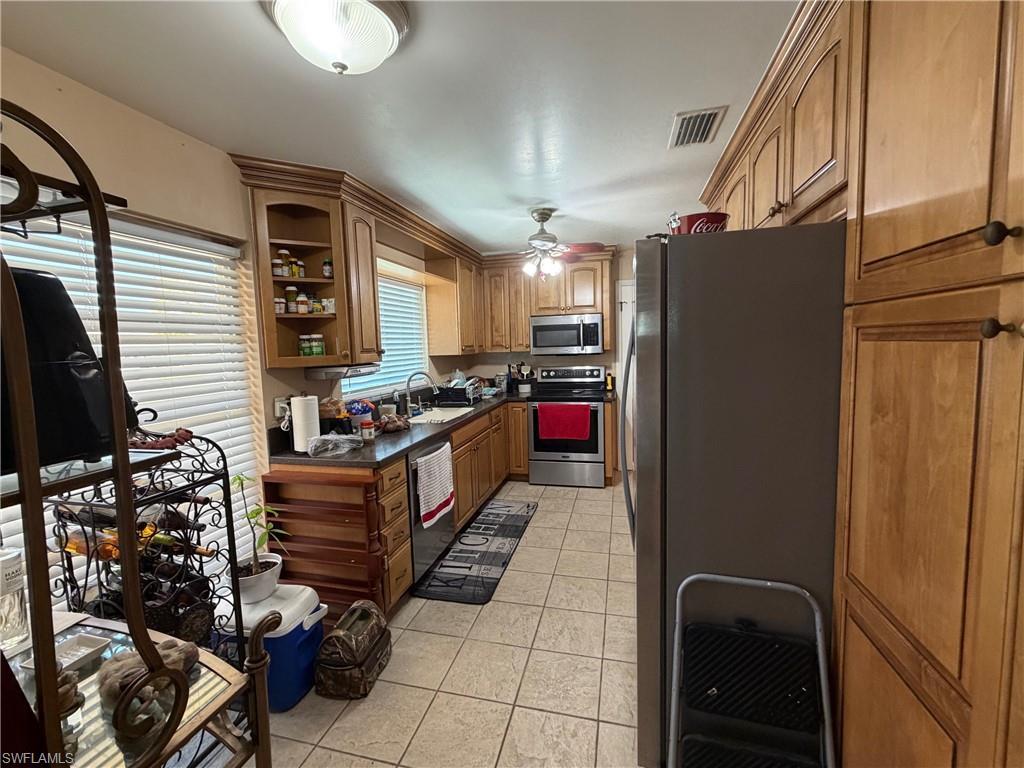 Image 4: Kitchen with stainless steel appliances, wood finish cabinetry, light tile patterned floors, dark countertops, and open shelves