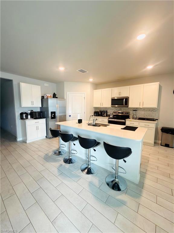 Image 2: Kitchen with white cabinets, a kitchen bar, stainless steel appliances, an island with sink, and tasteful backsplash