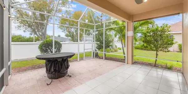 Image 4: Spacious screened patio area featuring both tiled and paved sections, with a ceiling fan and outdoor string lights