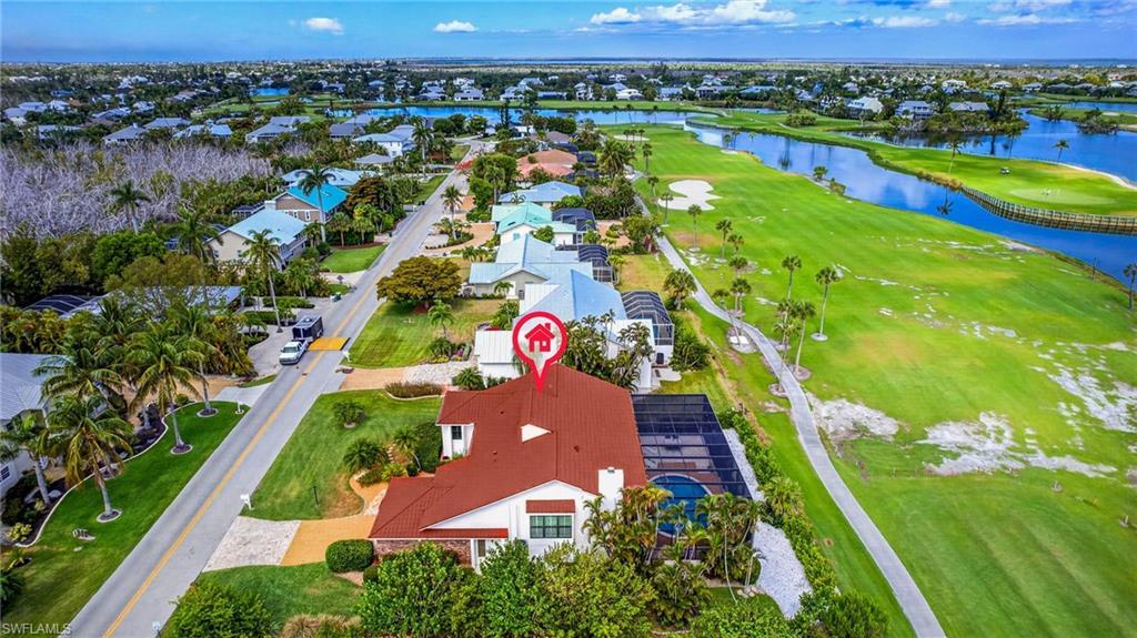 Image 2: White exterior home with a red tile roof, featuring a screened-in pool area, lush green landscaping, and proximity to a golf course and water features