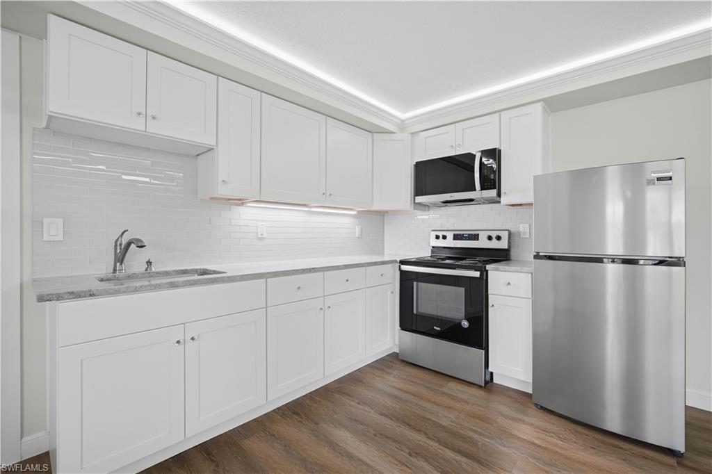 Image 4: Kitchen featuring white shaker-style cabinetry, light-toned countertops, a glass subway tile backsplash, stainless steel appliances, and wood-finish flooring