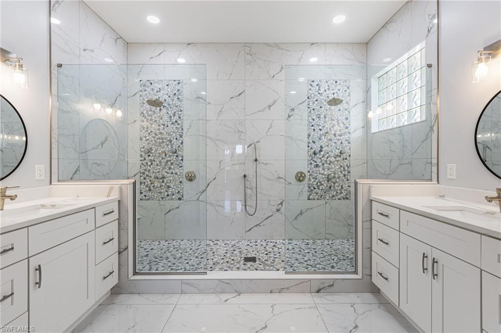 Image 1: The completely reimagined primary bathroom feels more like a private spa retreat, featuring his-and-hers quartz-topped vanities, a luxurious shower with dual heads, body sprays, and a handheld wand, all enclosed in seamless glass. Floor-to-ceiling porcelain walls and a striking listello add a designer touch, while custom cabinetry with pull-out drawers delivers impressive storage with style to spare.