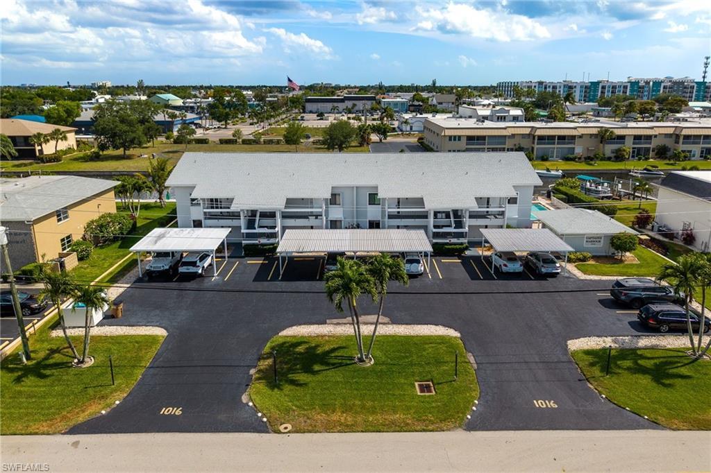 Image 1: Multi-story building featuring covered parking, a paved driveway, and mature palm trees