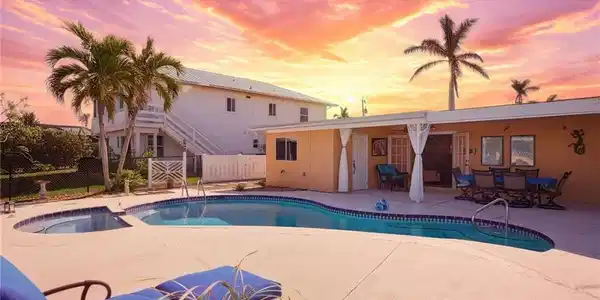 Image 2: Outdoor living space featuring a freeform swimming pool with integrated spa, expansive concrete patio, and a stucco-finish home exterior with French doors