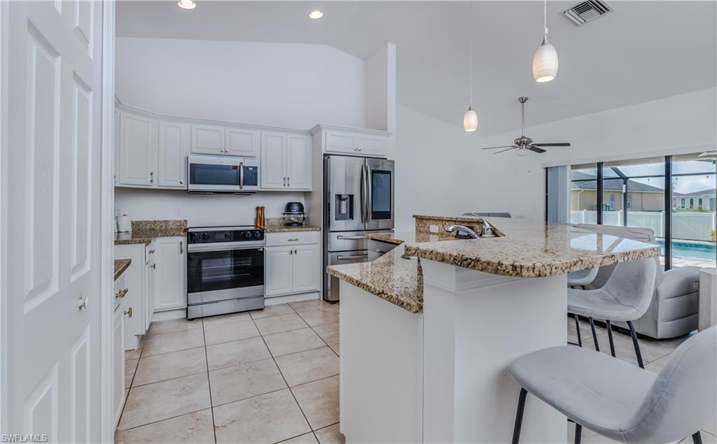 Image 3: Open-concept kitchen featuring granite countertops, stainless steel appliances, white cabinetry, and tile flooring