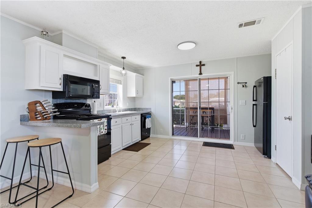 Image 2: Kitchen featuring light-finish cabinetry, black appliances, stone-finish countertops, and tile flooring