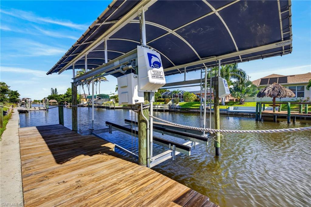 Image 2: Waterfront dock with a covered boat lift, featuring a wood-plank deck, canal access, and a clear blue sky overhead