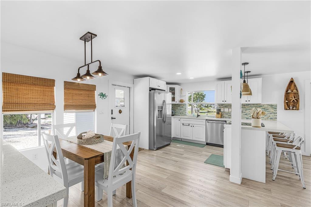 Image 2: Open-concept living space with wood-finish flooring, white cabinetry, stainless steel appliances, a multi-tone tile backsplash, and a dining area with a linear pendant light