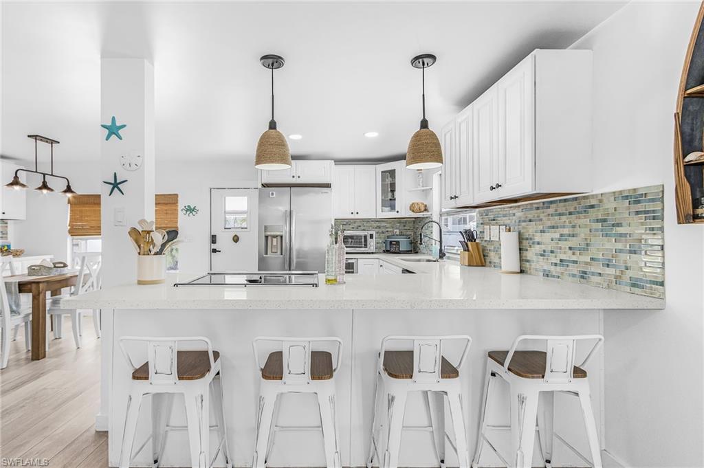 Image 3: Kitchen featuring a white countertop island with integrated cooktop, pendant lighting, stainless steel refrigerator, white cabinetry, and a mosaic tile backsplash
